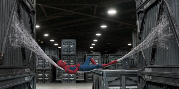 Spider-Man, Superheld im Spinnenkostüm, in einer Hängematte aus Spinnenfäden zwischen zwei Containern. Spider-Man, Superheld im Spinnenkostüm, in einer Hängematte aus Spinnenfäden zwischen zwei Containern.