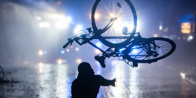 Eine Person wirft im Hamburger Schanzenviertel ein Fahrrad in Richtung von Wasserwerfern Eine Person wirft im Hamburger Schanzenviertel ein Fahrrad in Richtung von Wasserwerfern