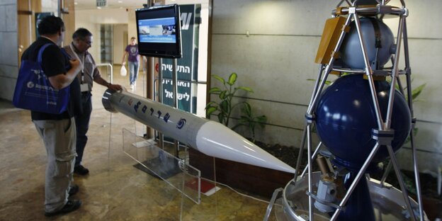 Zwei Menschen stehen vor einer Rakete Zwei Menschen stehen vor einer Rakete