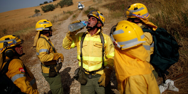 Feuerwehrmänner trinken aus einer Flasche.