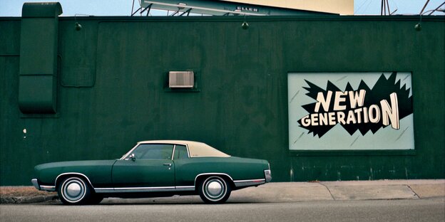 Ein grünes Auto steht vor einer grünen Wand, an der ein Werbeplakat mit der Aufschrit „New Generation“ hängt Ein grünes Auto steht vor einer grünen Wand, an der ein Werbeplakat mit der Aufschrit „New Generation“ hängt