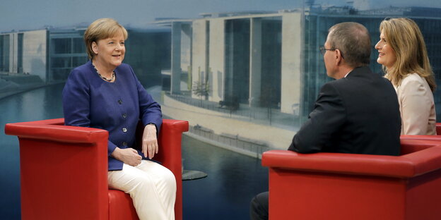 Angela Merkel sitzt in einem roten Sessel, gegenüber von Thomas Baumann und Tina Hassel Angela Merkel sitzt in einem roten Sessel, gegenüber von Thomas Baumann und Tina Hassel