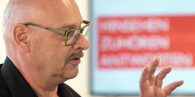 Ein Mann mit Brille spricht. Im Hintergrund steht: „Hinsehen, zuhören, antworten“ Ein Mann mit Brille spricht. Im Hintergrund steht: „Hinsehen, zuhören, antworten“
