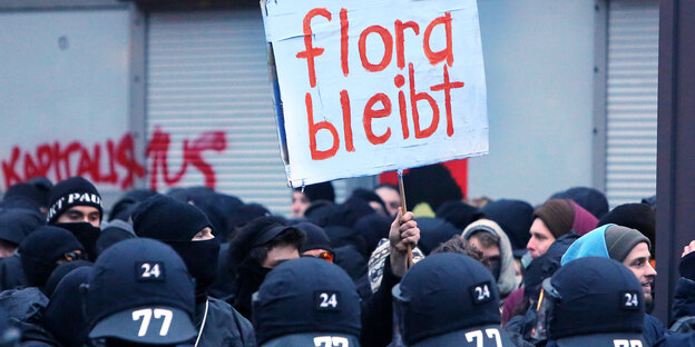 Viele Polizisten vor Demonstranten, die ein Schild mit der Aufschrift "Flora bleibt" halten Viele Polizisten vor Demonstranten, die ein Schild mit der Aufschrift "Flora bleibt" halten