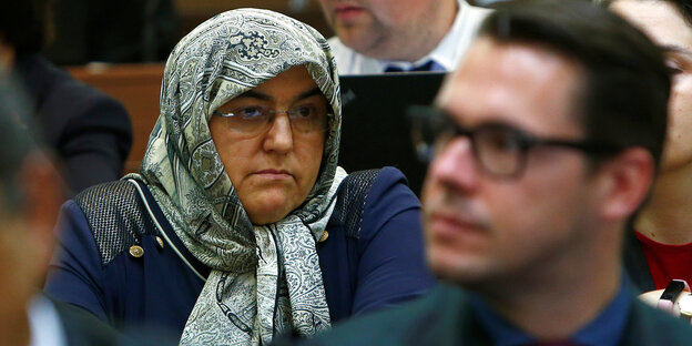 Eine Frau mit Kopftuch sitzt zwischen anderen Menschen Eine Frau mit Kopftuch sitzt zwischen anderen Menschen