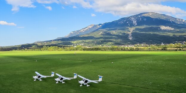 Drei Flugzeuge stehen auf einer Wiese nebeneinander. Im Hintergrund ein Berg Drei Flugzeuge stehen auf einer Wiese nebeneinander. Im Hintergrund ein Berg
