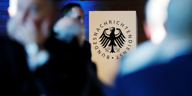 Das BND-Logo, davor unscharf mehrere Menschen Das BND-Logo, davor unscharf mehrere Menschen