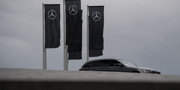 Ein schwarzes Auto fährt vor trübem Himmel unter drei schwarzen Mercedes-Flaggen vorbei Ein schwarzes Auto fährt vor trübem Himmel unter drei schwarzen Mercedes-Flaggen vorbei