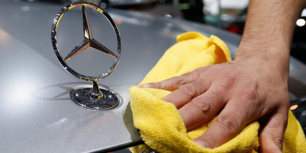 Eine Hand wischt mit einem gelben Tuch über die Motorhaube eines Mercedes Eine Hand wischt mit einem gelben Tuch über die Motorhaube eines Mercedes
