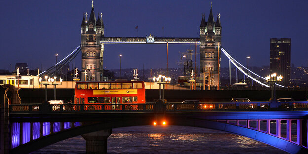 Ein roter Doppeldeckerbus fährt über eine Londoner Brücke in der Nacht Ein roter Doppeldeckerbus fährt über eine Londoner Brücke in der Nacht