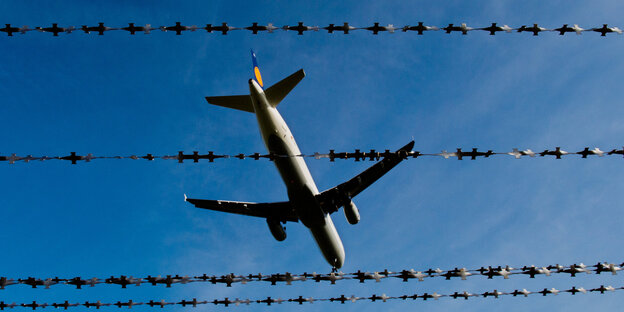 Ein Flugzeug fliegt über einen Stacheldrahtzaun Ein Flugzeug fliegt über einen Stacheldrahtzaun