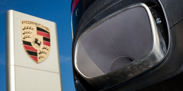Der Auspuff eines Porsche Cayenne neben dem Logo von Porsche Der Auspuff eines Porsche Cayenne neben dem Logo von Porsche