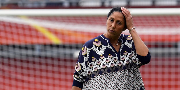 eine Frau fasst sich mit der linken Hand an den Kopf, im Hintergrund ein Fußballtor eine Frau fasst sich mit der linken Hand an den Kopf, im Hintergrund ein Fußballtor