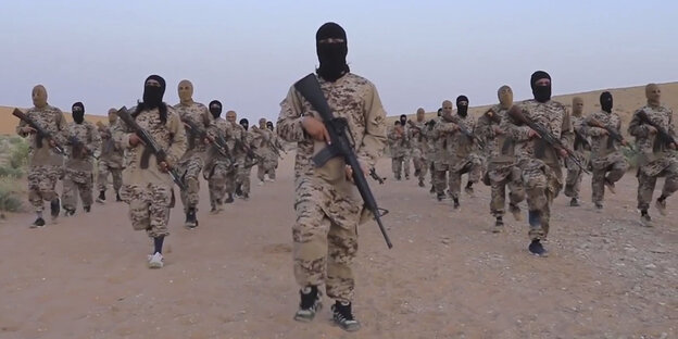 Vermummte Soldaten mit Gewehren marschieren auf Sand Vermummte Soldaten mit Gewehren marschieren auf Sand