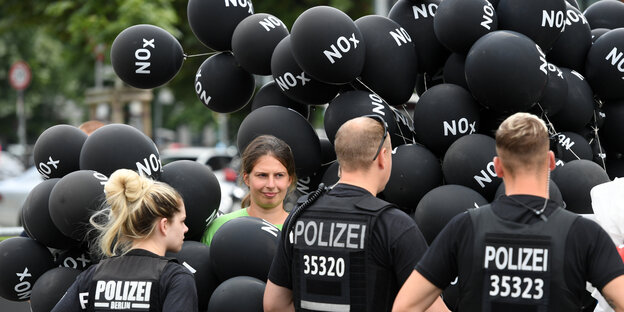 Polizisten stehen vor einer Frau mit vielen schwarzen Luftballons mit der Aufschrift NOx Polizisten stehen vor einer Frau mit vielen schwarzen Luftballons mit der Aufschrift NOx
