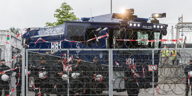 ein Wasserwerfer hinter einem mit Natodrahrt bewehrten Zaun ein Wasserwerfer hinter einem mit Natodrahrt bewehrten Zaun