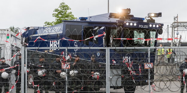 ein Wasserwerfer hinter einem mit Natodrahrt bewehrten Zaun