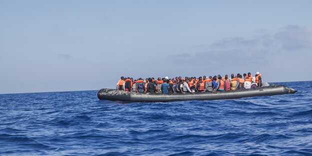 ein großes Schlauchboot voller Menschen, von denen die meisten Schwimmwesten tragen ein großes Schlauchboot voller Menschen, von denen die meisten Schwimmwesten tragen