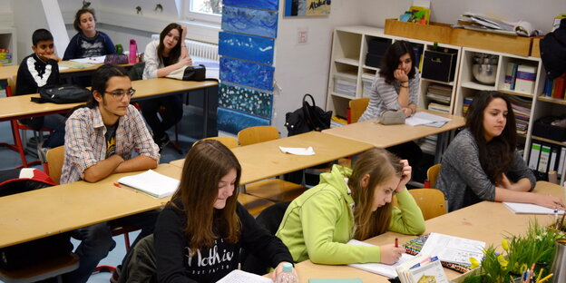 Schuler und Schülerinnen sitzen in ihren Schultischen Schuler und Schülerinnen sitzen in ihren Schultischen