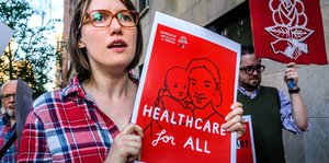 Eine junge Frau hält ein Plakat, auf dem steht auf Englisch Krankenversicherung für alle