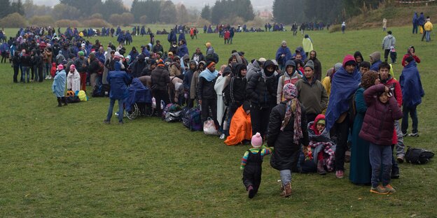 Eine größere Menschenmenge warten auf einer Wiese Eine größere Menschenmenge warten auf einer Wiese