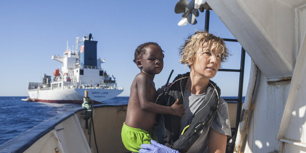 Eine blonde Frau an Bord eines Schiffes hält ein schwarzes Baby auf dem Arm Eine blonde Frau an Bord eines Schiffes hält ein schwarzes Baby auf dem Arm