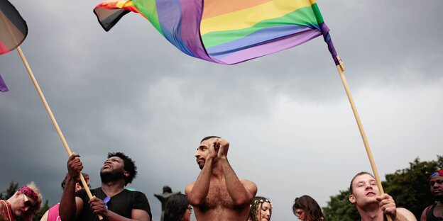 Drei Männer, zwei davon schwenken eine Regenbogenfahne