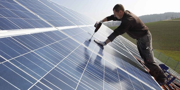 Mann montiert Solarzellen auf ein Dach Mann montiert Solarzellen auf ein Dach