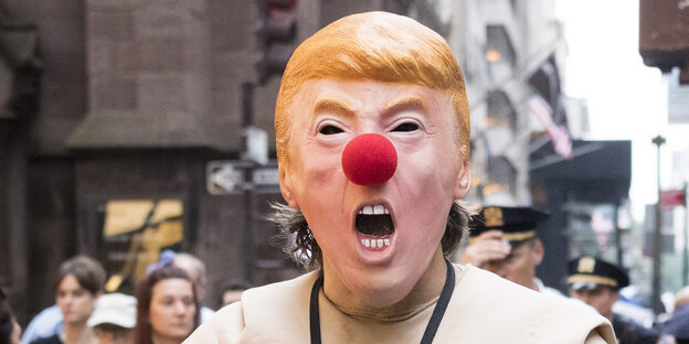 Ein Mensch trägt eine Maske mit einem verzerrten Gesicht des US-Präsidenten Donald Trump Ein Mensch trägt eine Maske mit einem verzerrten Gesicht des US-Präsidenten Donald Trump