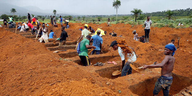 Arbeiter in Freetown heben in roter Erde Gräber aus Arbeiter in Freetown heben in roter Erde Gräber aus