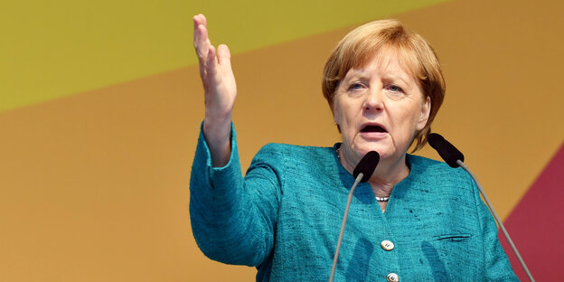 Angela Merkel auf einem Podium im Porträt, ihre rechte Hand zeigt in die Höhe Angela Merkel auf einem Podium im Porträt, ihre rechte Hand zeigt in die Höhe