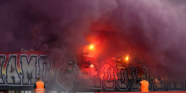 Orange-leuchtende Flammen inmitten von riesigen Rauchwolken auf einer Fußball-Tribüne Orange-leuchtende Flammen inmitten von riesigen Rauchwolken auf einer Fußball-Tribüne