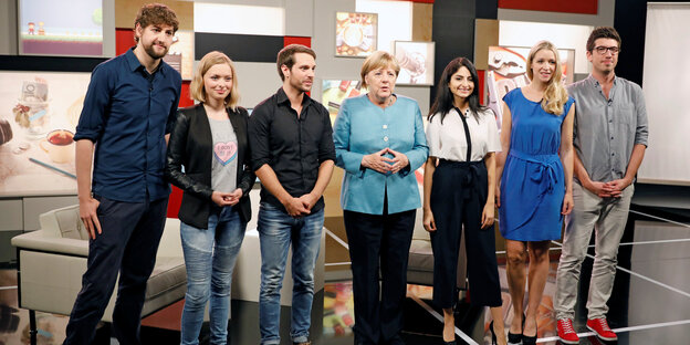 Sieben Frauen und Männer stehen nebeneinander in einem Fernsehstudio