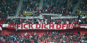 Fans halten in einem Fußballstadion Transparente mit der Aufschrift "Untergrabung von 50+1", "Eventisierung", "Kollektivstrafen" und "Fick dich DFB!" in die Höhe