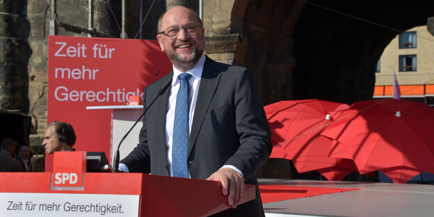 Ein Mann im Anzug vor roten Bannern Ein Mann im Anzug vor roten Bannern