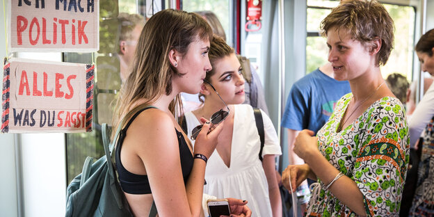 Drei junge Frauen stehen in einem Bahnwaggon und diskutieren