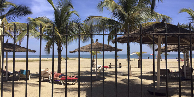 Touristen liegen am Strand unter Palmen, davor ein Gitterzaun Touristen liegen am Strand unter Palmen, davor ein Gitterzaun