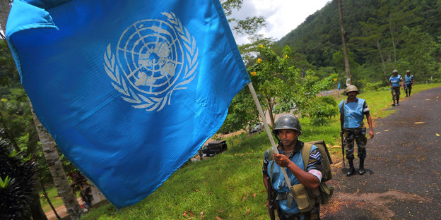 Ein Soldat trägt eine blaue UNO-Flagge