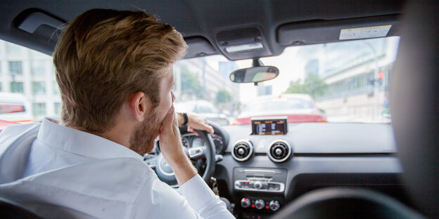 Ein Mann sitzt im Auto. Durch die Windschutzscheibe sieht man einen Stau vor ihm Ein Mann sitzt im Auto. Durch die Windschutzscheibe sieht man einen Stau vor ihm