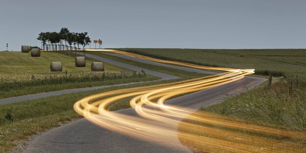 Bei Dämmerung läuft eine Lichtspur über eine Landstraße. Bei Dämmerung läuft eine Lichtspur über eine Landstraße.