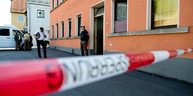 Absperrband vor einem Haus, dahinter ein Polizist Absperrband vor einem Haus, dahinter ein Polizist