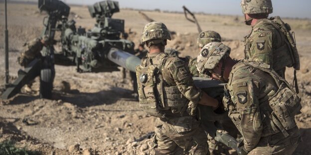 Soldaten schieben an einer Kriegsmaschine herum Soldaten schieben an einer Kriegsmaschine herum