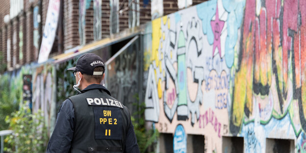 Ein Polizist vor einer mit Grafitti besprühten Wand Ein Polizist vor einer mit Grafitti besprühten Wand