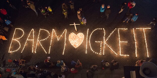 Kerzen formen das Wort Barmherzigkeit. Menschen stehen drum herum Kerzen formen das Wort Barmherzigkeit. Menschen stehen drum herum