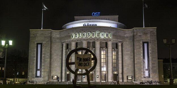 Die Berliner Volksbühne bei Nacht und beleuchtet. An der Radskulptur vor dem Haus ein Transpi mit der Aufschrift "Für immer und Dich" Die Berliner Volksbühne bei Nacht und beleuchtet. An der Radskulptur vor dem Haus ein Transpi mit der Aufschrift "Für immer und Dich"