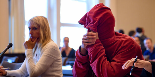 Ein Mann mit rotem Pullover hat die Kapuze übers Gesicht gezogen Ein Mann mit rotem Pullover hat die Kapuze übers Gesicht gezogen