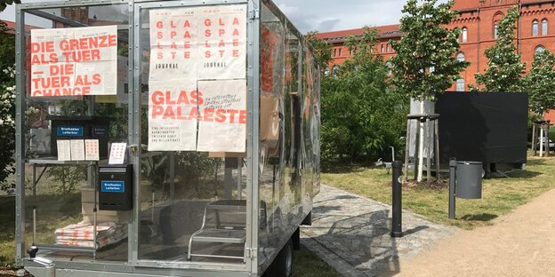 Ein Anhänger aus Glas mit Plakaten vor einem Backsteingebäude Ein Anhänger aus Glas mit Plakaten vor einem Backsteingebäude