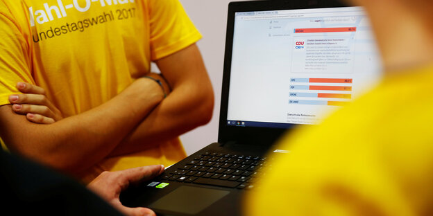 Zwei Menschen in gelben T-Shirts neben einem Laptop, auf dem der Wahl-O-Mat gerade gespielt wird Zwei Menschen in gelben T-Shirts neben einem Laptop, auf dem der Wahl-O-Mat gerade gespielt wird