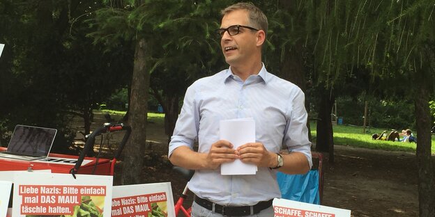 Stefan Liebich steht redend mit einem Zettel in der Hand vor einigen Wahlplakaten.