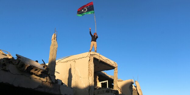 Ein Mensch steht auf einer Ruine und schwenkt eine Flagge Ein Mensch steht auf einer Ruine und schwenkt eine Flagge